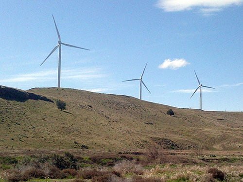 Three wind turbines on a grassy hill with blue skies