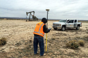 RRC surveyor with equipment in field in front of an oil pump and RRC company truck
